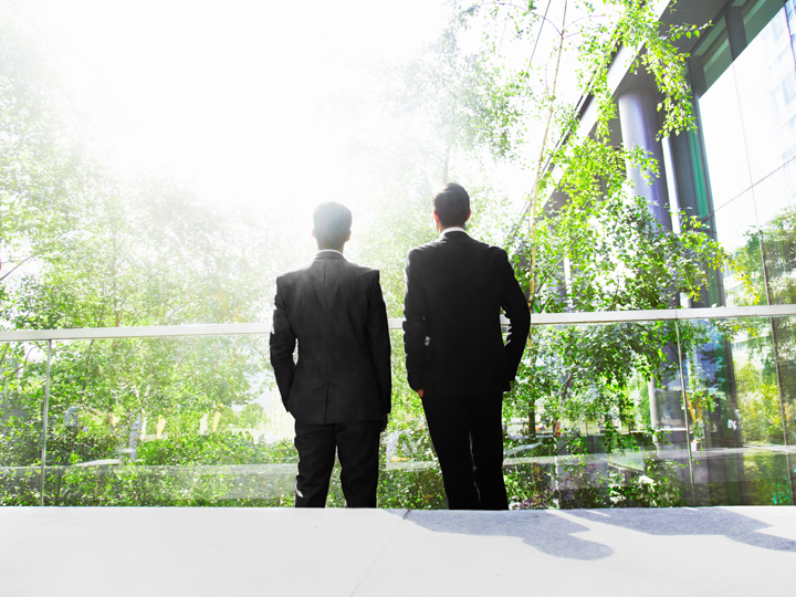 Two men in suits standing surrounded by greenery